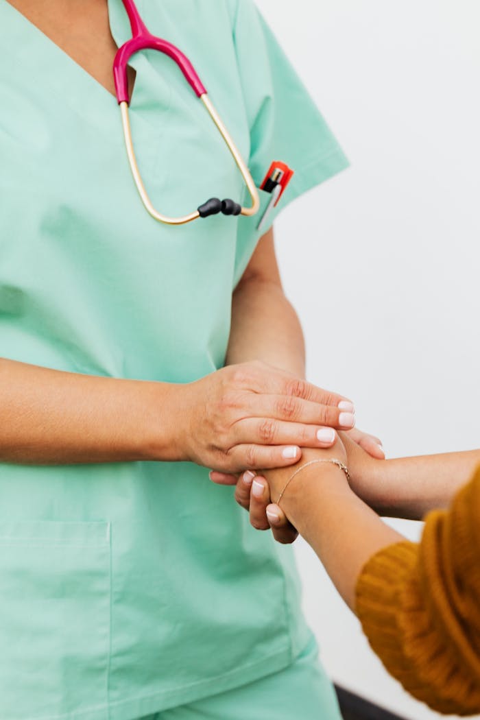 A nurse in green scrubs gently clasps a patients hand, offering support.